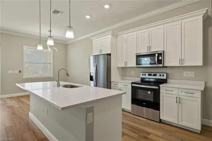 Kitchen with stainless steel appliances, white cabinetry, crown molding, a center island with sink, and light stone counters