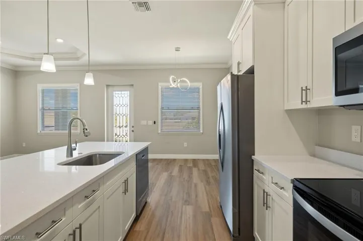 Kitchen featuring white cabinets, crown molding, light wood-style floors, stainless steel appliances, and light stone countertops