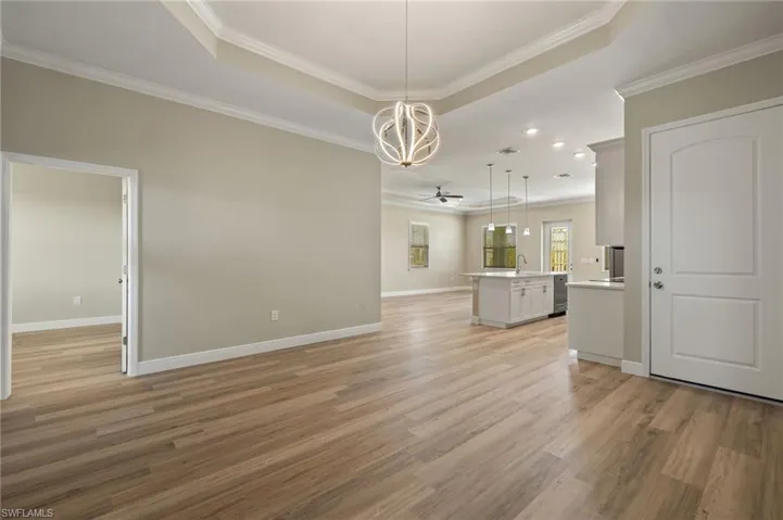Unfurnished dining area featuring crown molding, light wood-style floors, ceiling fan, and a raised ceiling