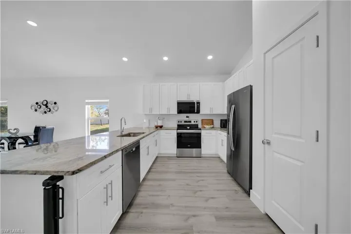 Kitchen with stainless steel appliances, white cabinets, light stone countertops, recessed lighting, and a peninsula