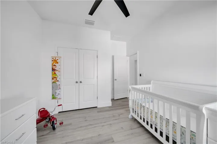 Bedroom with a crib, light wood finished floors, a closet, and a ceiling fan