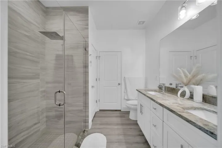 Full bath featuring double vanity, a shower stall, and light wood-style flooring