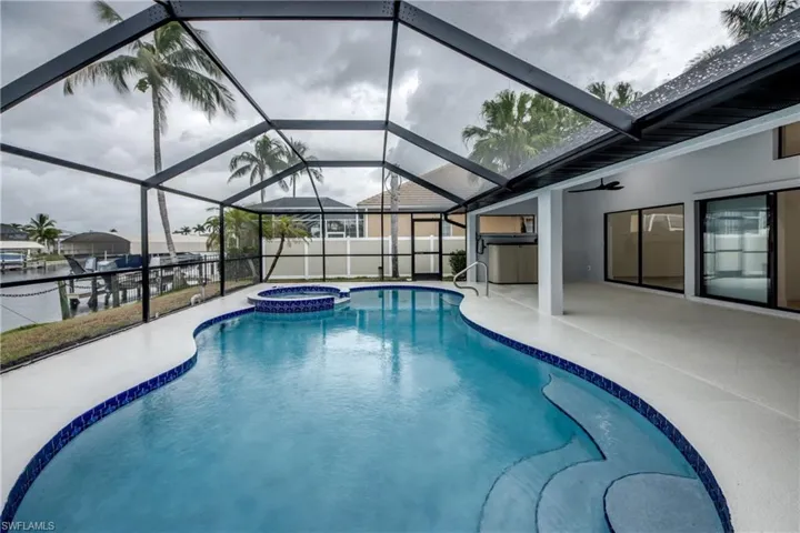 View of pool with glass enclosure, an in ground hot tub, and a patio area