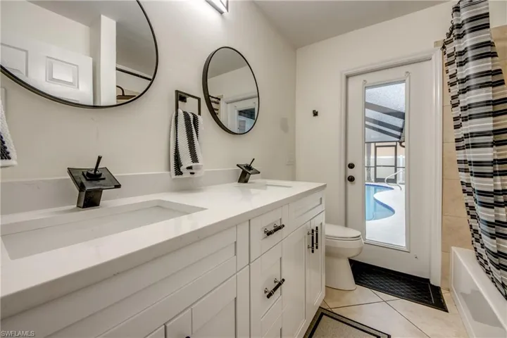 Full bathroom featuring tile flooring, dual vanity, toilet, and shower / tub combo with curtain