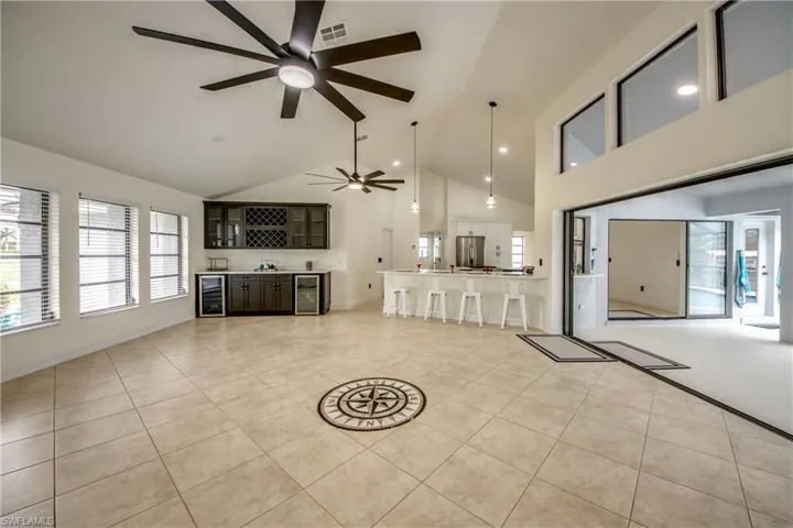 Unfurnished living room with high vaulted ceiling, ceiling fan, beverage cooler, and light tile floors
