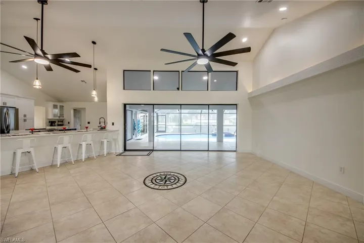 Unfurnished living room with high vaulted ceiling, ceiling fan, and light tile floors