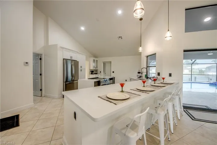 Kitchen featuring stainless steel appliances, pendant lighting, high vaulted ceiling, a breakfast bar area, and white cabinetry