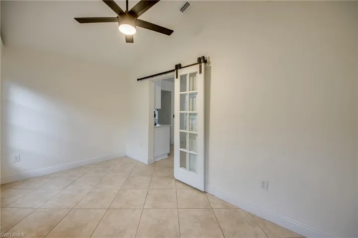 Tiled empty room with a barn door, ceiling fan, and lofted ceiling