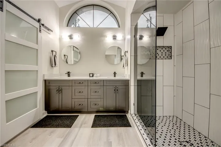 Bathroom featuring tiled shower, lofted ceiling, hardwood / wood-style flooring, oversized vanity, and dual sinks