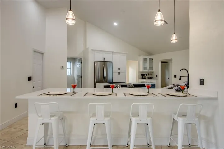 Kitchen featuring kitchen peninsula, hanging light fixtures, a kitchen bar, white cabinetry, and stainless steel refrigerator