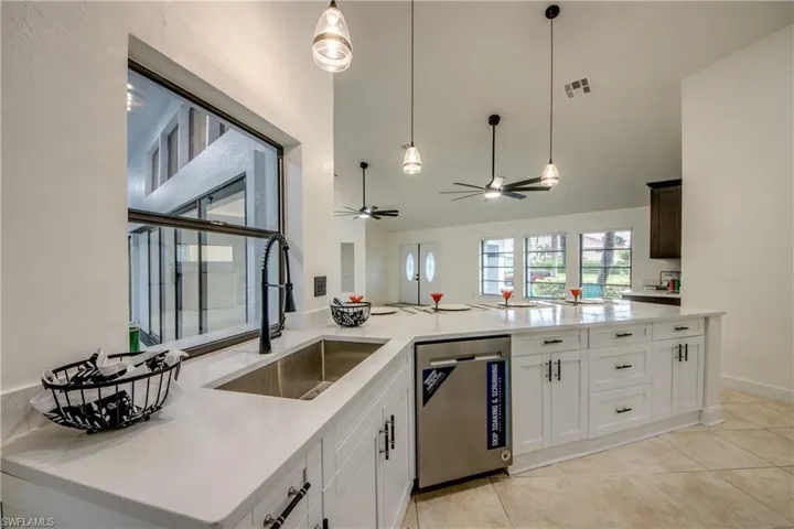 Kitchen with decorative light fixtures, dishwasher, ceiling fan, sink, and light tile floors
