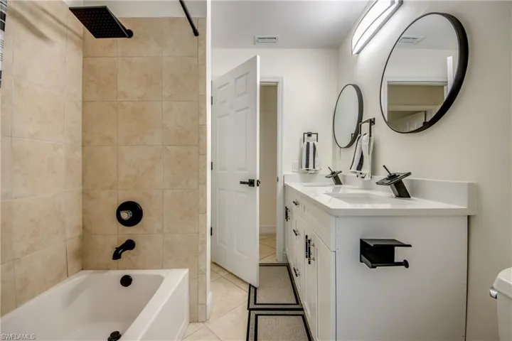 Full bathroom with double sink vanity, toilet, tiled shower / bath combo, and tile floors