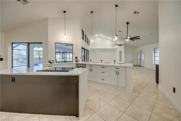 Kitchen featuring decorative light fixtures, high vaulted ceiling, white cabinets, and ceiling fan