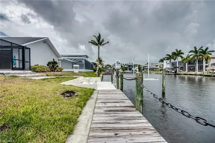 View of dock featuring glass enclosure, a lawn, and a water view