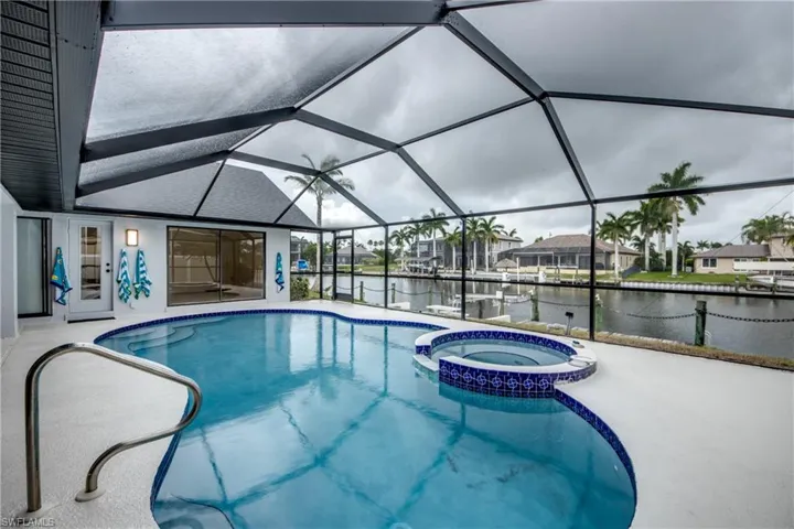 View of swimming pool with a patio area, a water view, glass enclosure, and an in ground hot tub