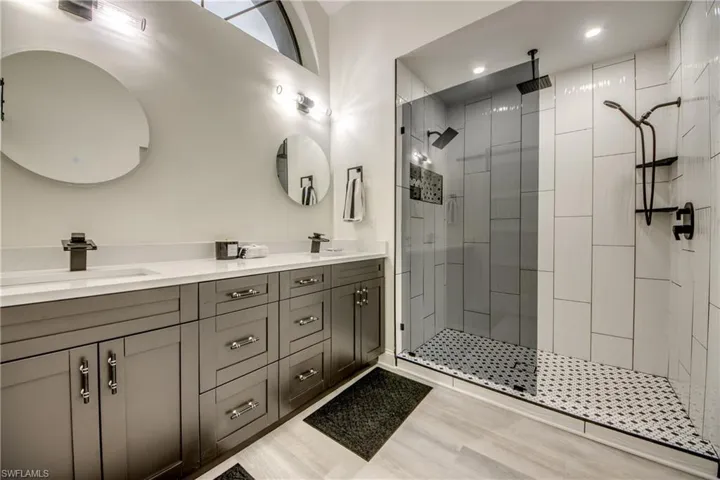 Bathroom featuring an enclosed shower, vanity with extensive cabinet space, and dual sinks
