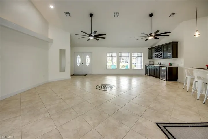 Unfurnished living room featuring high vaulted ceiling, wine cooler, ceiling fan, and light tile flooring