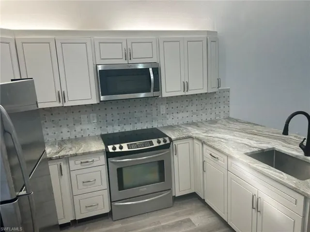 Kitchen with stainless steel appliances, light stone counters, light wood-type flooring, decorative backsplash, and a peninsula