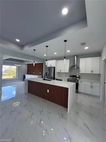Kitchen with wall chimney range hood, light countertops, white cabinetry, visible vents, and electric stove