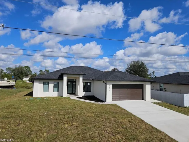 Prairie-style home with an attached garage, driveway, stucco siding, and a front lawn