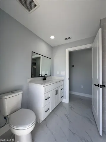 Bathroom featuring toilet, vanity, marble finish floor, and visible vents