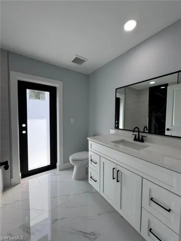 Bathroom featuring visible vents, baseboards, toilet, vanity, and marble finish floor