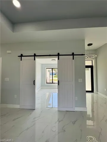 Empty room with marble finish floor, a barn door, and baseboards