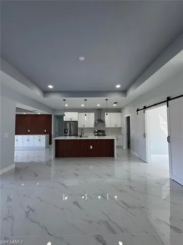Unfurnished living room featuring marble finish floor, recessed lighting, baseboards, and a barn door