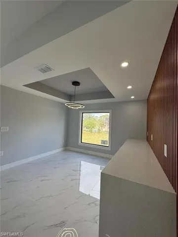 Unfurnished dining area with a tray ceiling, visible vents, recessed lighting, marble finish floor, and baseboards