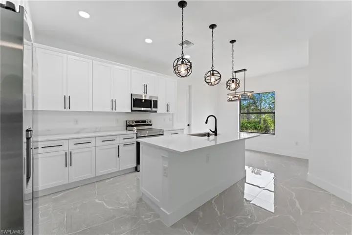 Kitchen featuring hanging light fixtures, stainless steel appliances, white cabinetry, and a kitchen island with sink