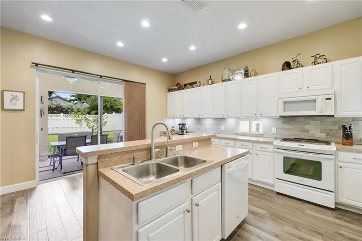 Kitchen featuring a center island with sink, tasteful backsplash, white cabinets, sink, and white appliances