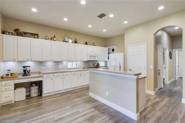 Kitchen with a kitchen island with sink, white appliances, white cabinetry, and backsplash