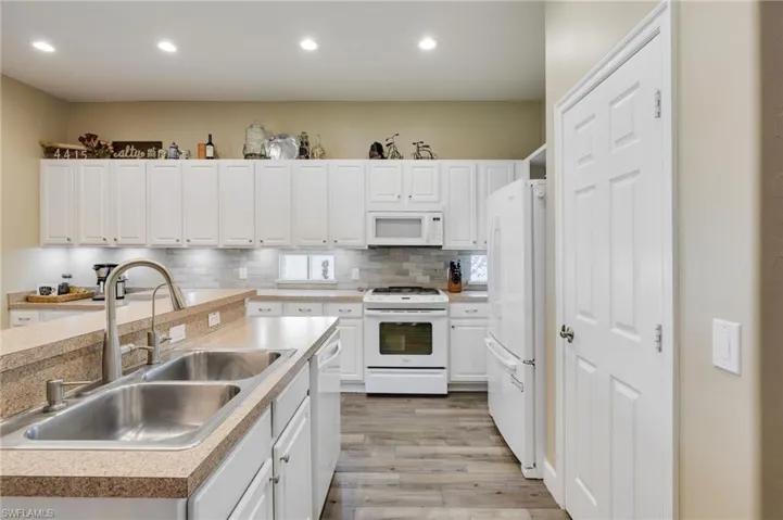 Kitchen featuring light hardwood / wood-style flooring, white appliances, backsplash, sink, and white cabinets