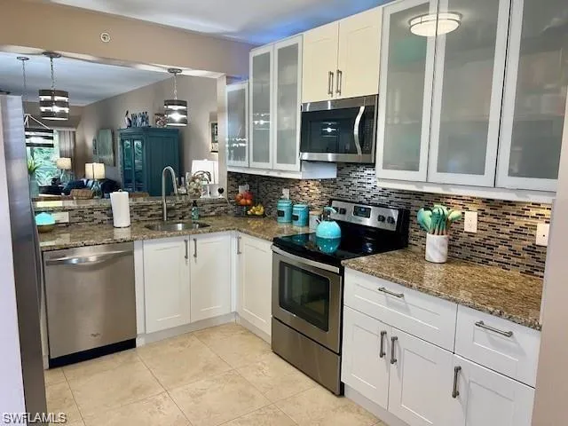 Kitchen with white cabinetry, appliances with stainless steel finishes, and dark stone counters