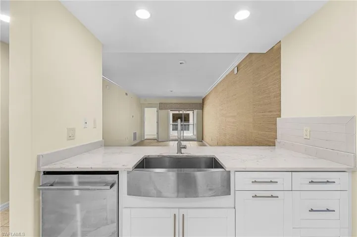 Kitchen featuring a stainless steel farmhouse sink, white shaker cabinetry, light-toned countertops, and a subway tile backsplash