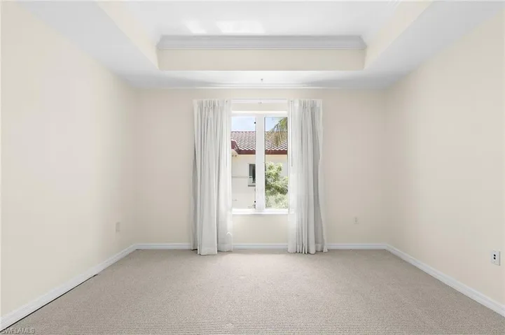 Recessed ceiling with layered trim, framed window with white curtains, light-toned carpet flooring, neutral wall paint, and white baseboards