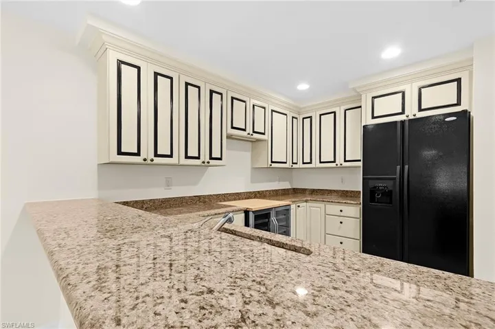 Kitchenette featuring extensive light-toned cabinetry with dark trim, complementing granite countertops, and a full-size black refrigerator