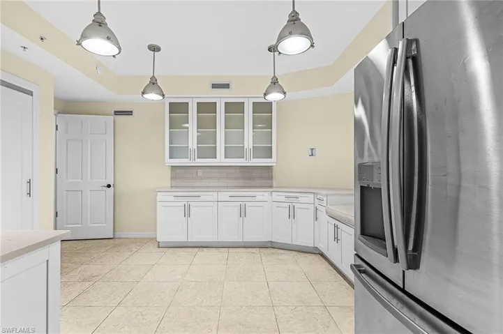 Stainless steel refrigerator featured in a kitchen with white cabinetry, light-toned countertops, and a subway tile backsplash