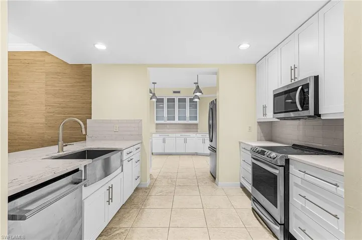 Kitchen featuring white shaker cabinetry, stainless steel appliances, light-toned countertops, and tile flooring