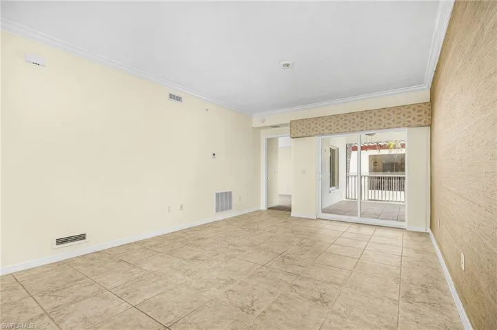 Spacious room featuring neutral-toned tile flooring, crown molding, and a full-wall sliding glass door opening to a private outdoor space