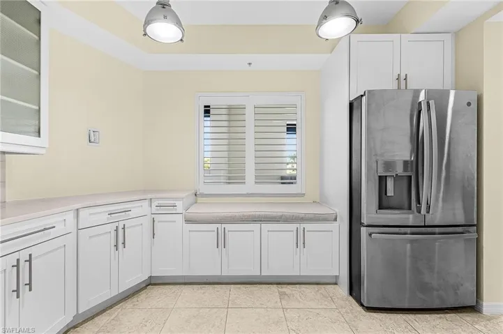 Kitchen area featuring a built-in window seat, white cabinetry with contemporary hardware, light-toned countertop, stainless steel refrigerator, and tiled flooring