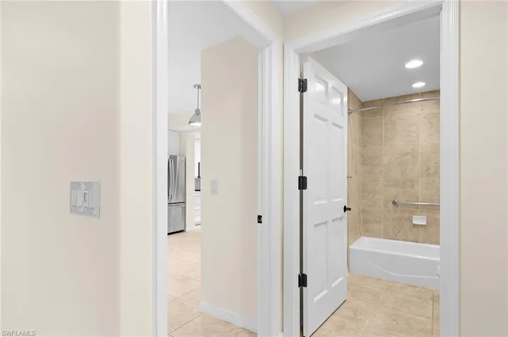 Bathroom featuring a white tub, light-toned tiled shower surround, recessed lighting, and a grab bar