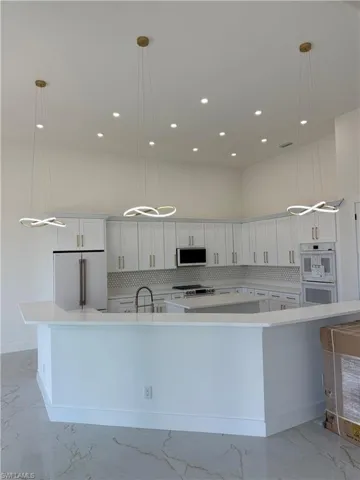 Kitchen with white appliances, light marble finish floors, a high ceiling, backsplash, and white cabinetry
