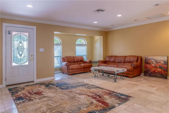 Living area with a wealth of natural light, visible vents, crown molding, and stone tile flooring