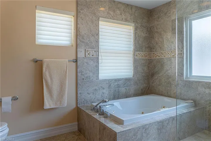 Full bath featuring toilet, a tub with jets, and baseboards