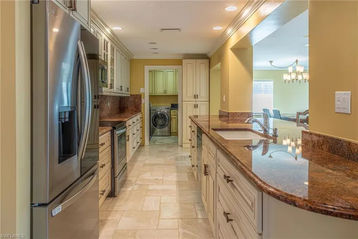 Kitchen with crown molding, stone tile flooring, cream cabinetry, stainless steel appliances, and a sink