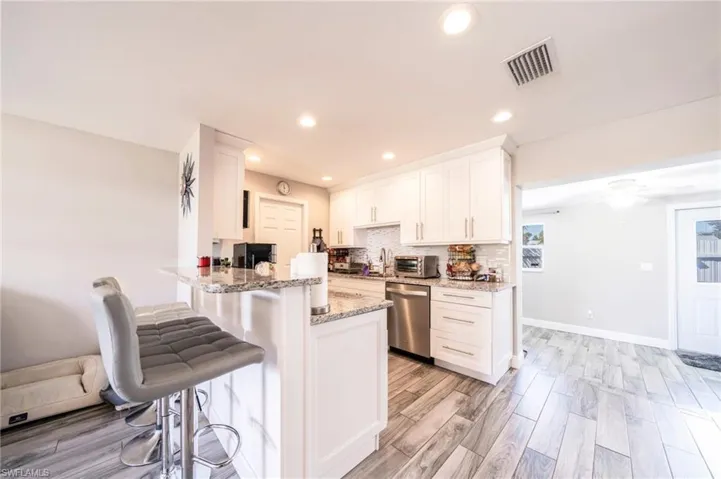 Kitchen featuring white cabinets, light stone counters, a kitchen breakfast bar, tasteful backsplash, and wood finish floors
