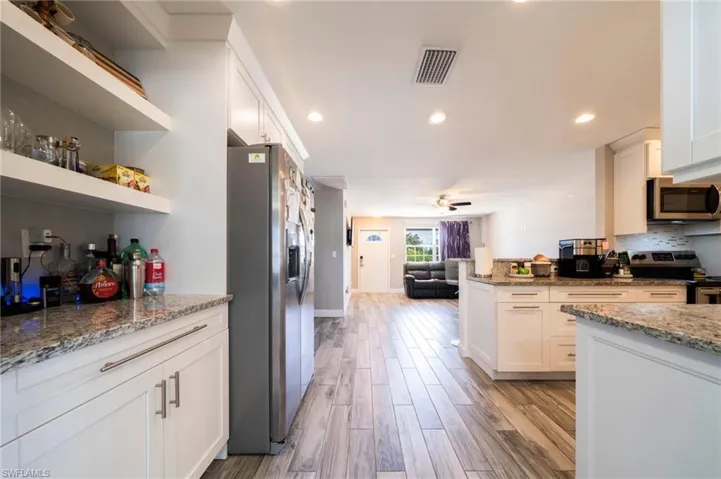 Kitchen with open shelves, light stone counters, open floor plan, white cabinets, and stainless steel appliances