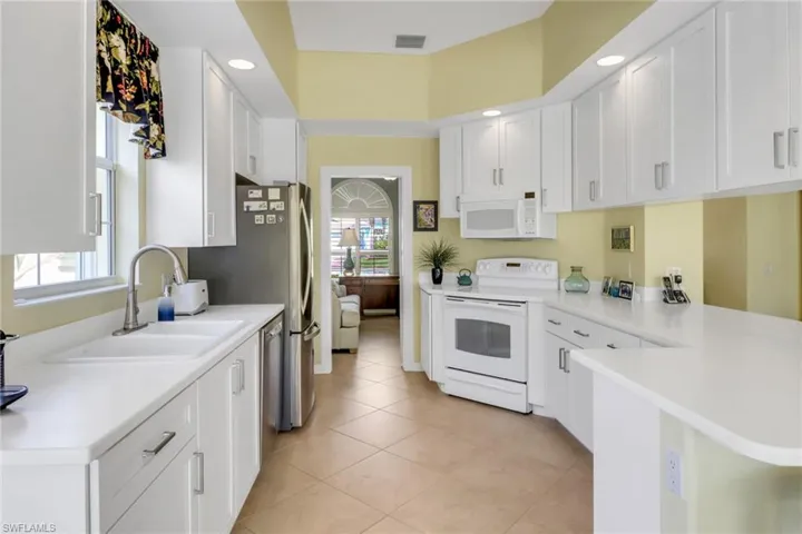 Kitchen featuring a peninsula, white appliances, a sink, visible vents, and white cabinets