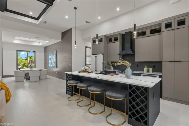 Kitchen with hanging light fixtures, a large island, light stone counters, and wall chimney exhaust hood
